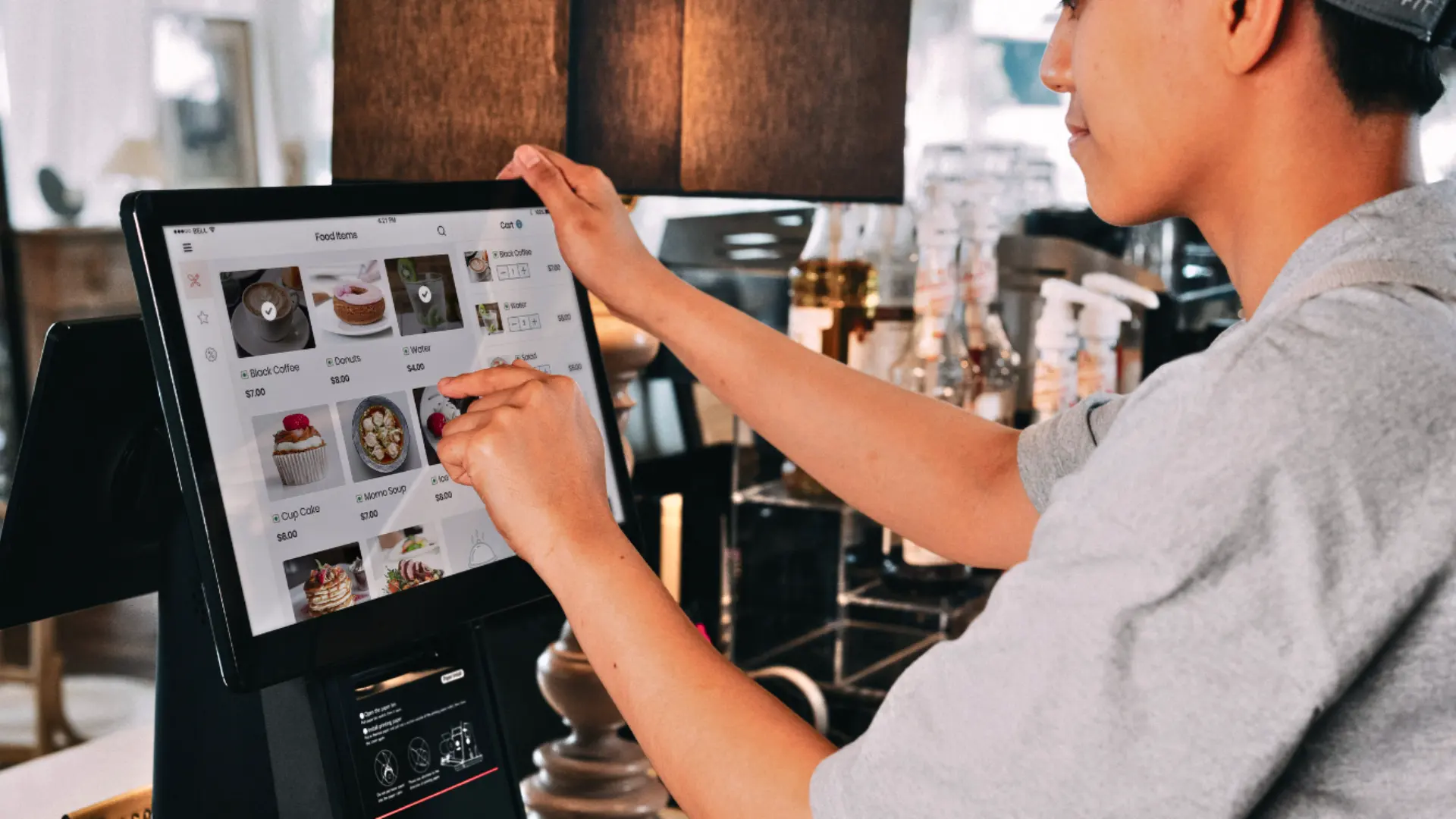 A cafe employee using a modern touch-screen POS system to manage food orders, demonstrating simple business technology.